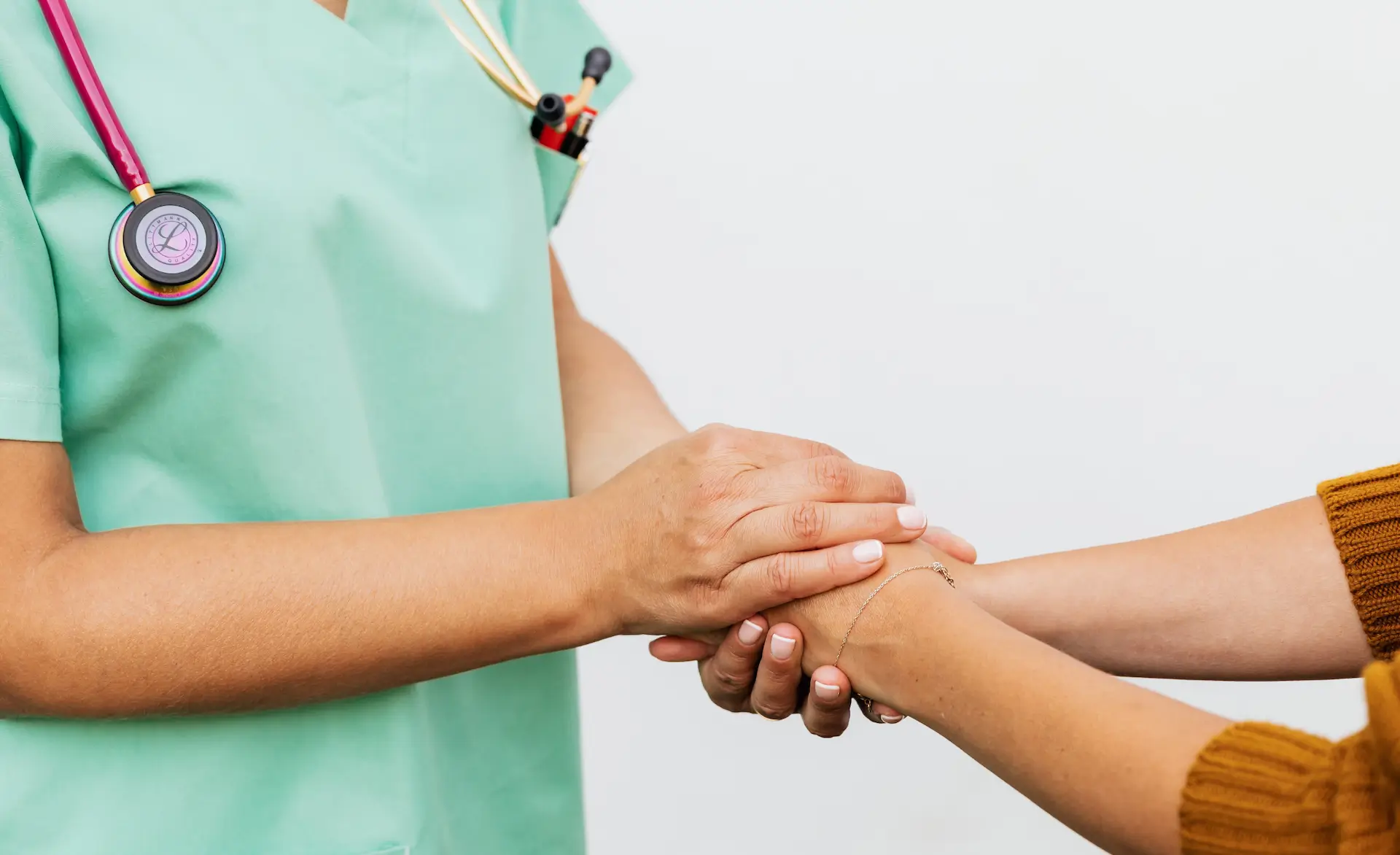 two people clasping hands. Only their arms and hands are visible. We can see one is a medical professional in green scrubs