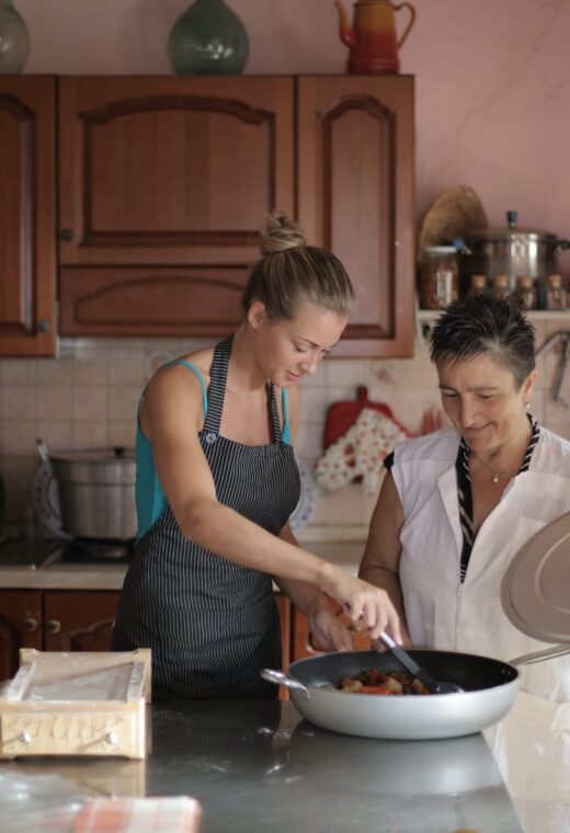 two women preparing a meal, one of them is stirring in a large pan