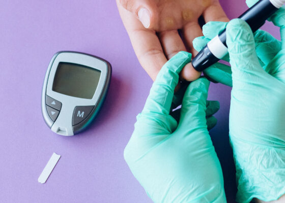 hands wearing green medical gloves holding some finger pricking equipment and pricing the hand of another person