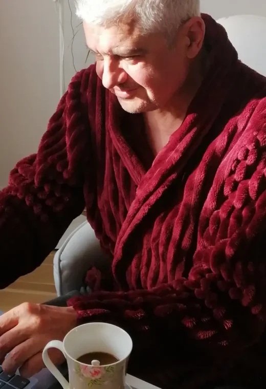 an older man wearing a red robe sat at a laptop