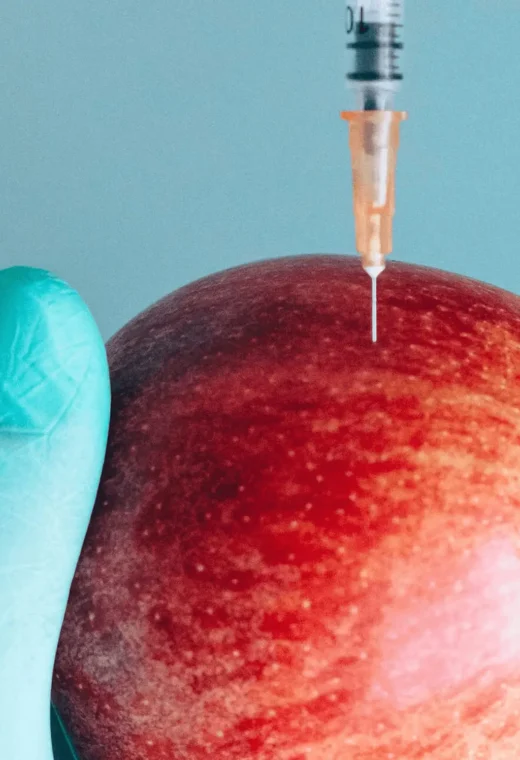 a hand wearing blue medical gloves holding an apple, with a needle in the apple