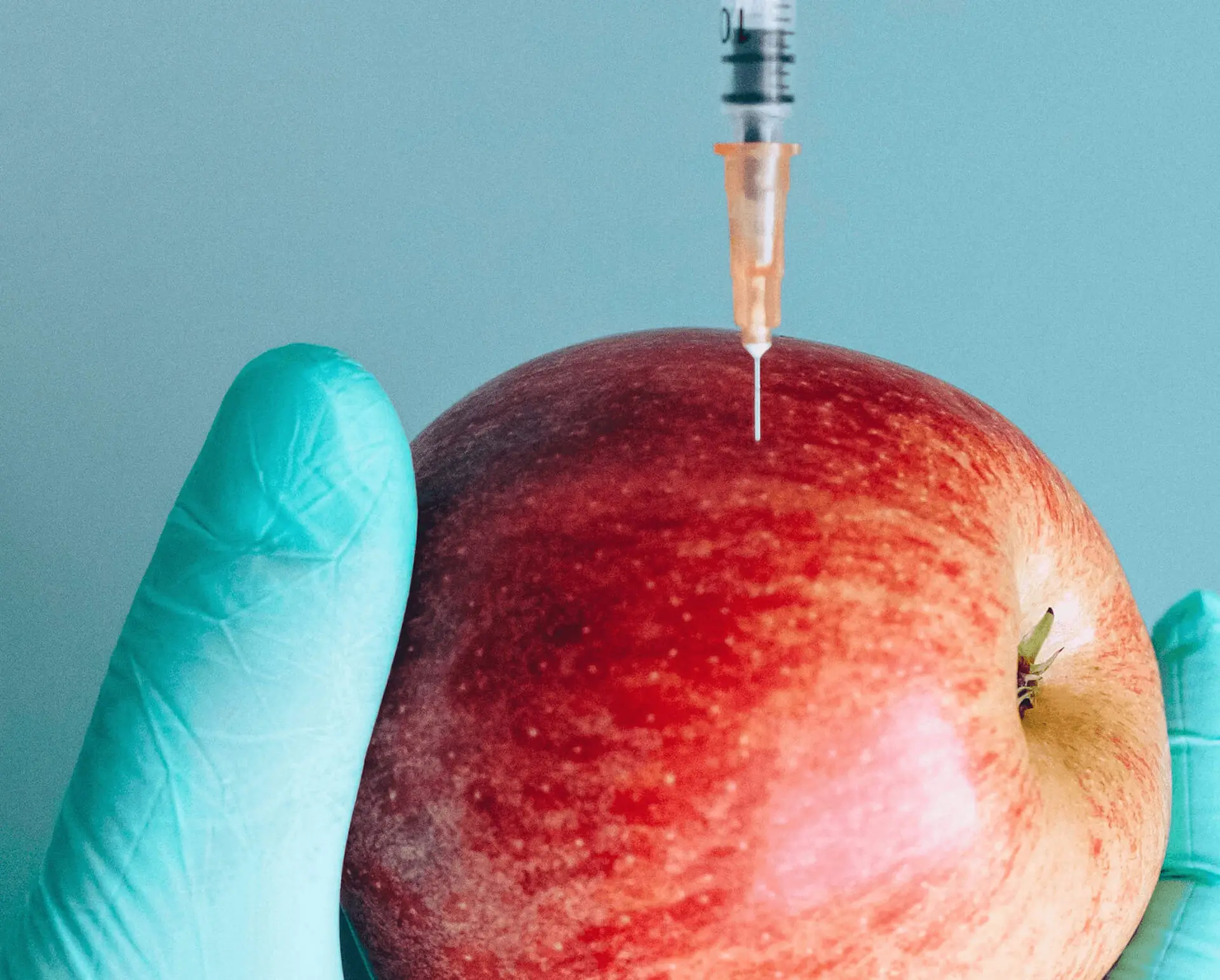 a hand wearing blue medical gloves holding an apple, with a needle in the apple