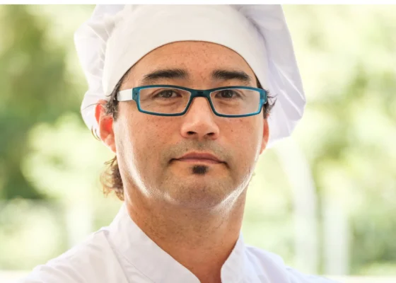 Man in black glasses looking at the camera.He is wearing chefs whites.