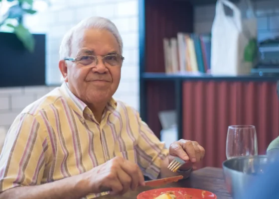 an older gentleman eating a meal while looking into the camera and smiling