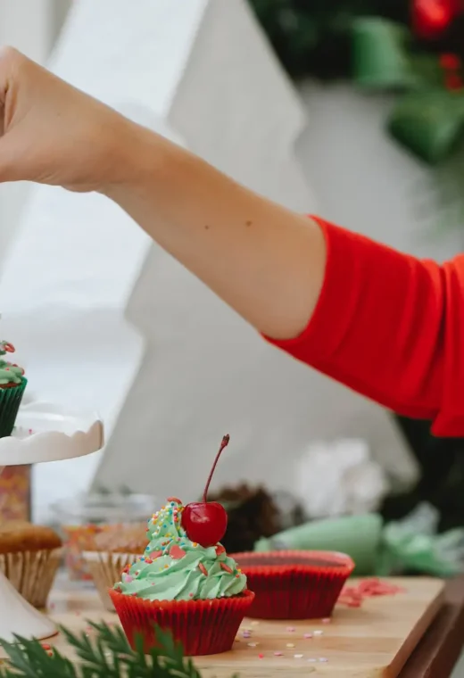 image of a hand putting a cherry on top of a Christmas themed cupcake