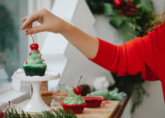 image of a hand putting a cherry on top of a Christmas themed cupcake