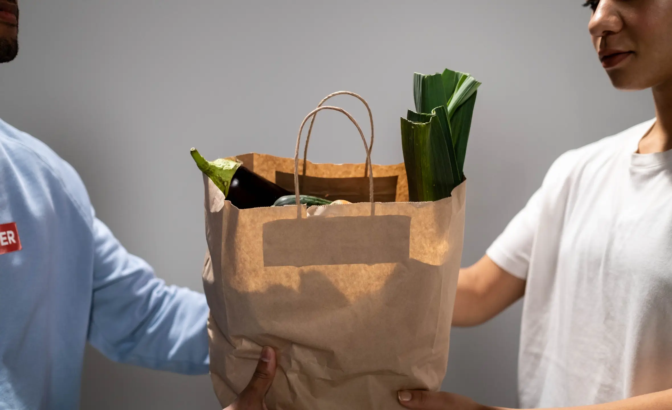 two people holding a brown paper bag with vegetables