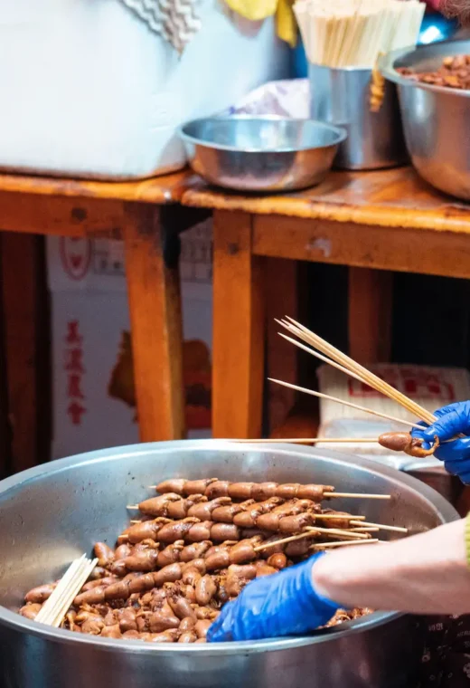 lady stood over a large cooking pot making a type of kebab skewer