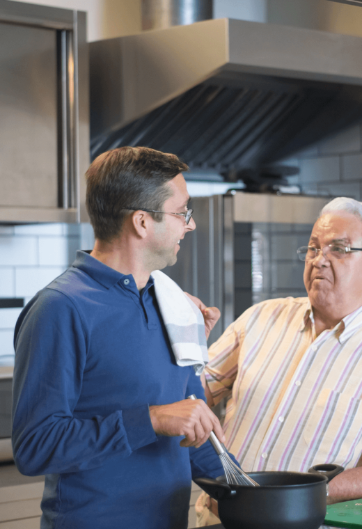 2 men cooking together, they are smiling and enjoying themselves