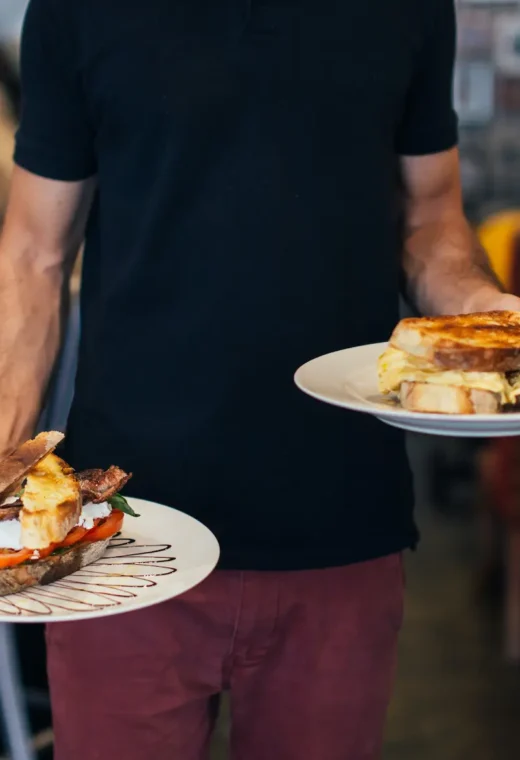 a man wearing black holding two plates of food