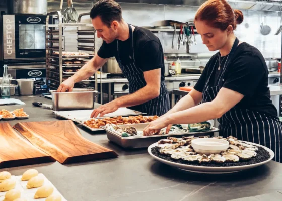 two caterers in a kitchen preparing meals in multiple dishes