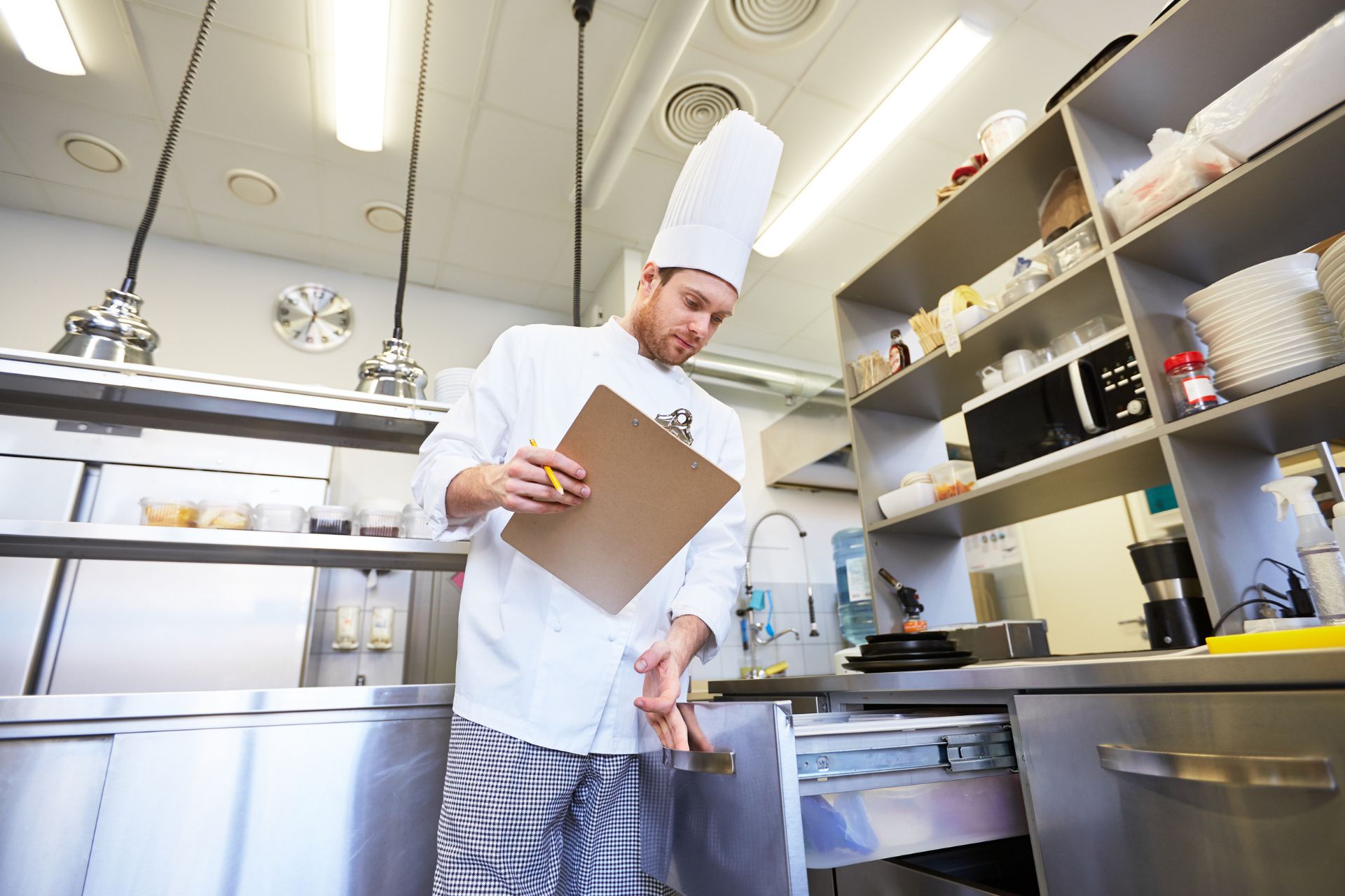 A chef with a clipboard looking in drawers in a kitchen for do agency chefs need a dbs check